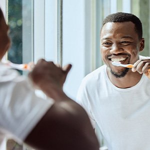 Man smiling while brushing his teeth in bathroom