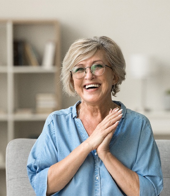 Senior woman with glasses smiling on couch at home.