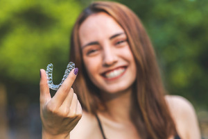 Woman smiling and holding up an Invisalign aligner
